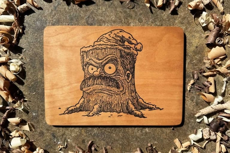 Carved wooden holiday card featuring a whimsical tree character with a face, crafted by Offerman Woo.